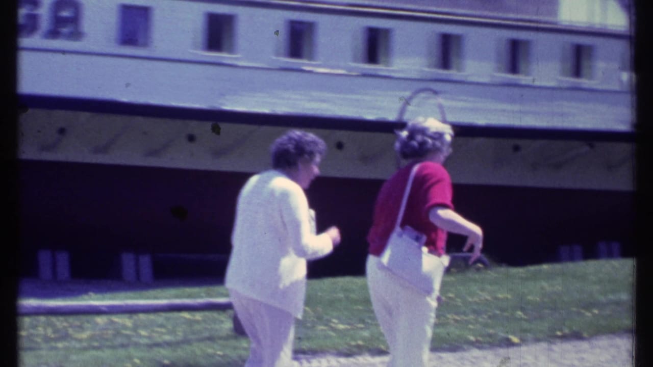 In Vermont 1984 home-movie footage, two older women walk past a docked riverboat, one wearing a red top and white pants.