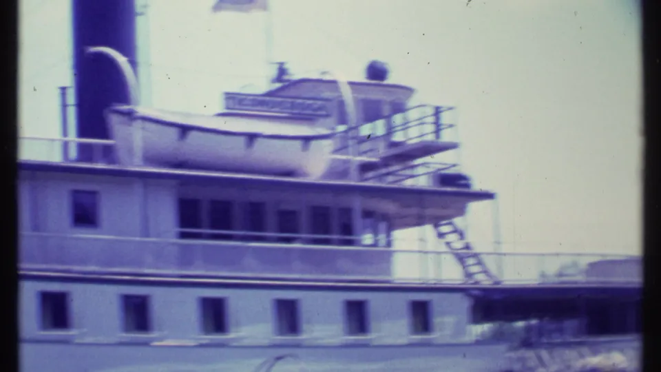 The riverboat fills the frame, showing railings, small windows, exterior stairs, and partially readable lettering on the upper deck.
