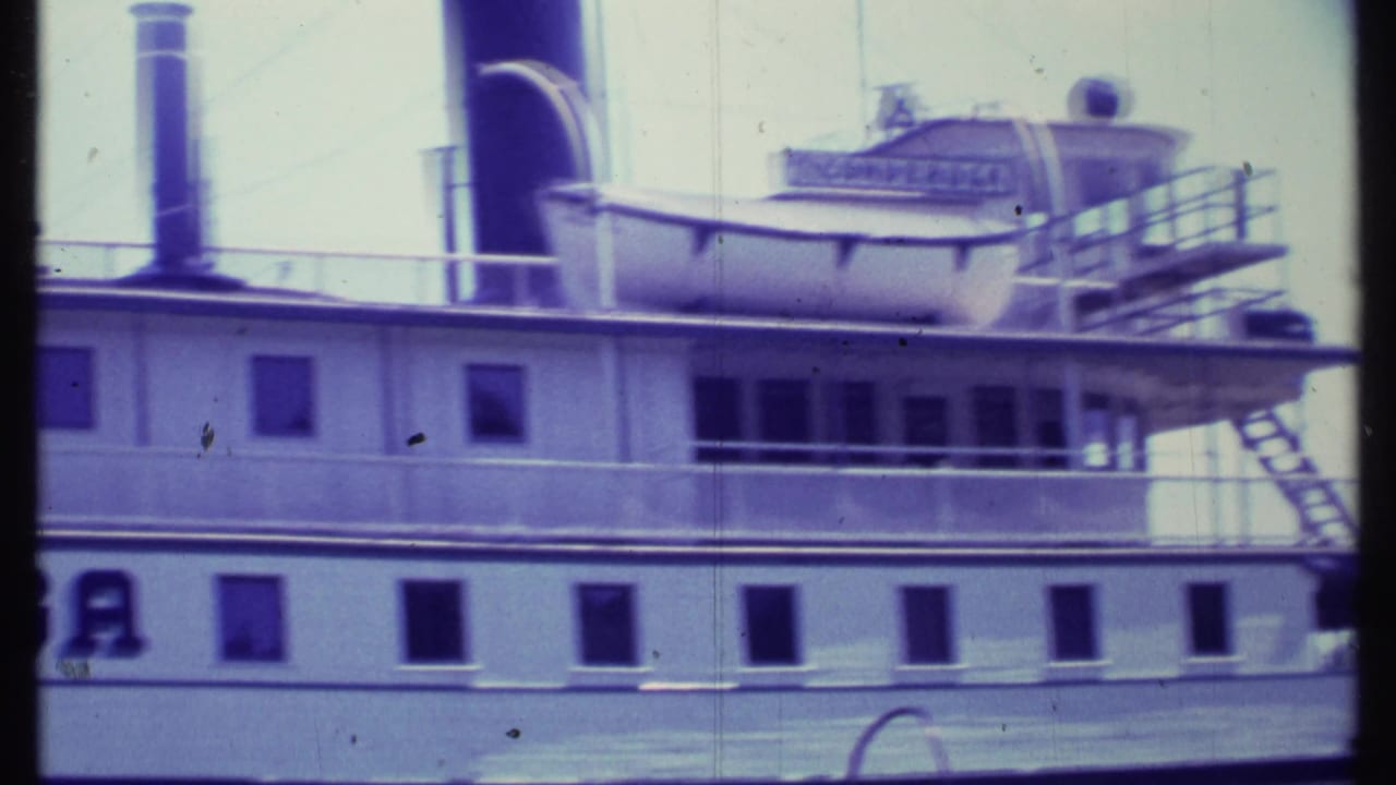 Close view of a white steamboat side with windows, railings, upper deck equipment, and part of the hull lettering.