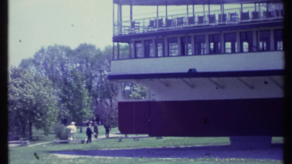 A wider 1984 Vermont view shows the boat at the dock edge, a grassy shoreline, trees, and a few distant people walking nearby.