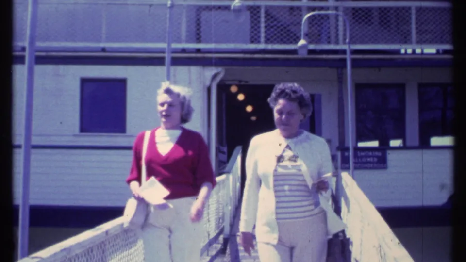 Two women in casual 1980s clothing walk side by side down a Vermont ramp, filmed in soft 8mm color.
