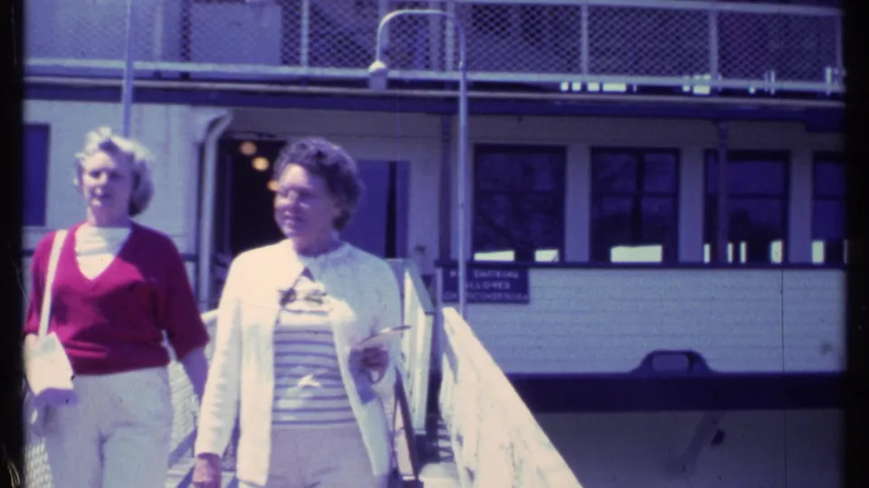 Near the end of the 1984 Vermont clip, the women pass close to the camera on a sunlit ramp outside a white building.