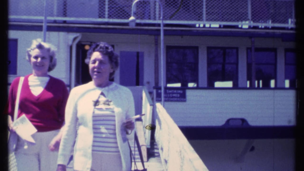 Two women walk along a dock beside a large boat structure.
