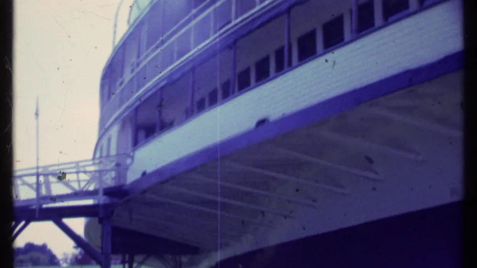 1984 Vermont home-movie frame showing the raised vessel side, underside supports, gangway, windows, and railings.