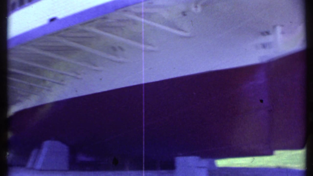 Close view of a red-and-white boat hull with underside deck details and film gate edges.