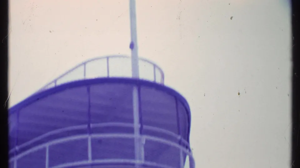 1984 Vermont 8mm frame showing a curved purple-tinted structure with a railing and vertical pole against a pale sky.