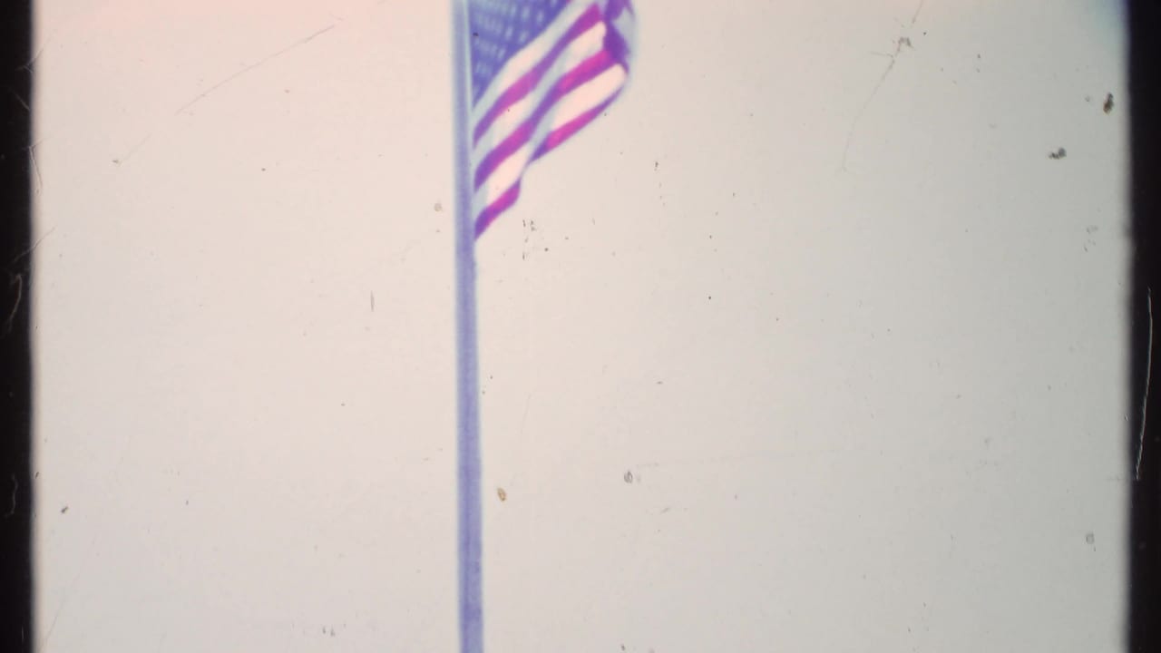 American flag waving from a tall pole against a pale sky.