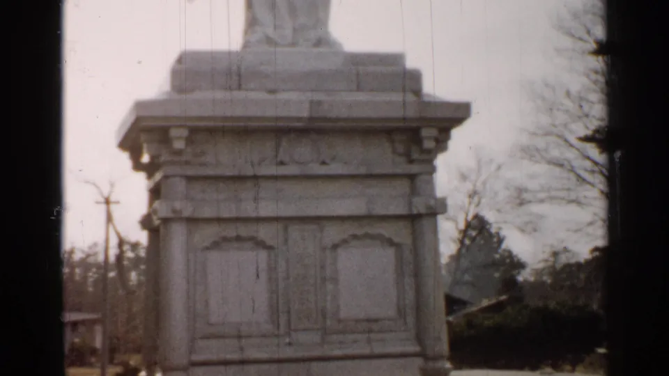 Final frame of the 1952 Japan home movie clip showing the monument pedestal, surrounding trees, and soft cloudy light.