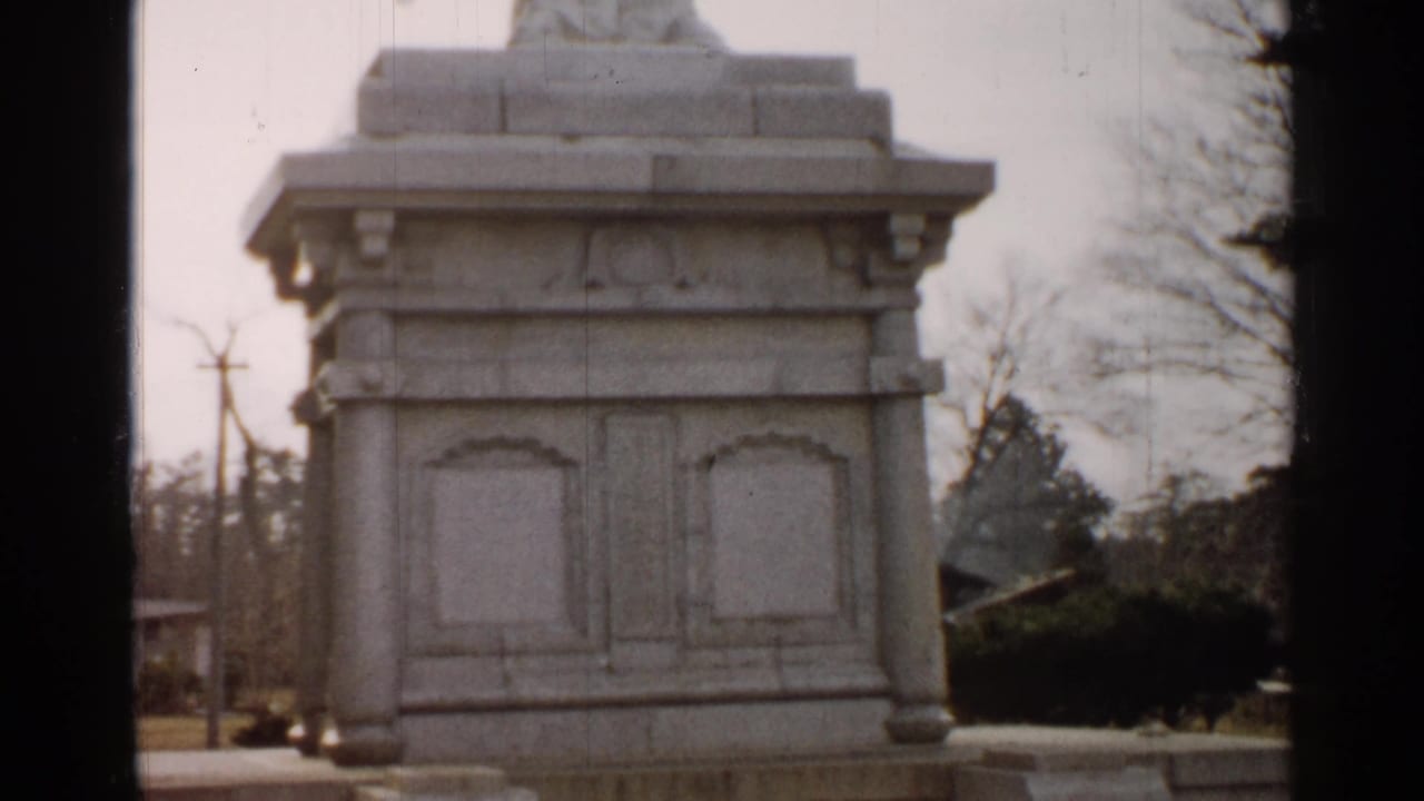 White stone pedestal seen close up with bare trees and utility poles behind it.