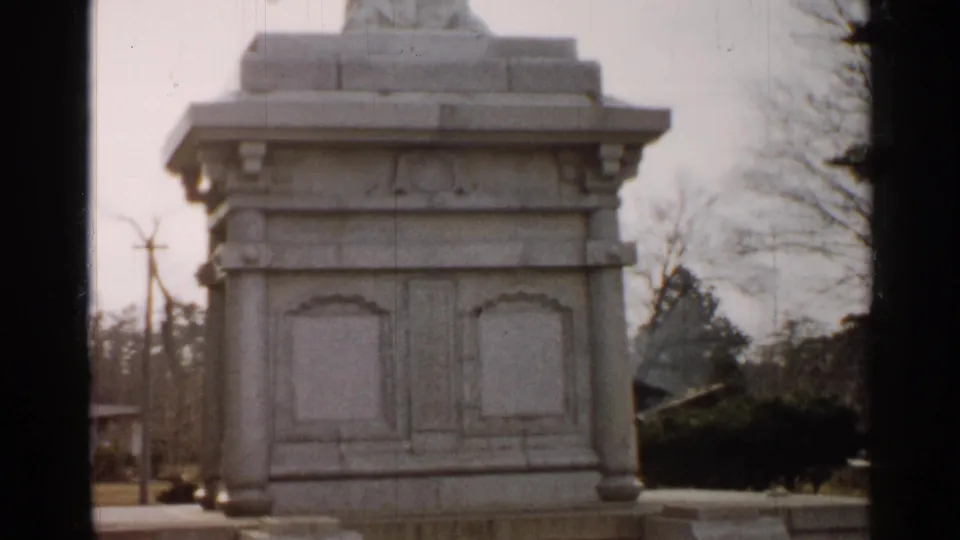 1952 8mm Japan frame showing the upper portion of a white stone pedestal outdoors, with bare trees and utility poles in the background.