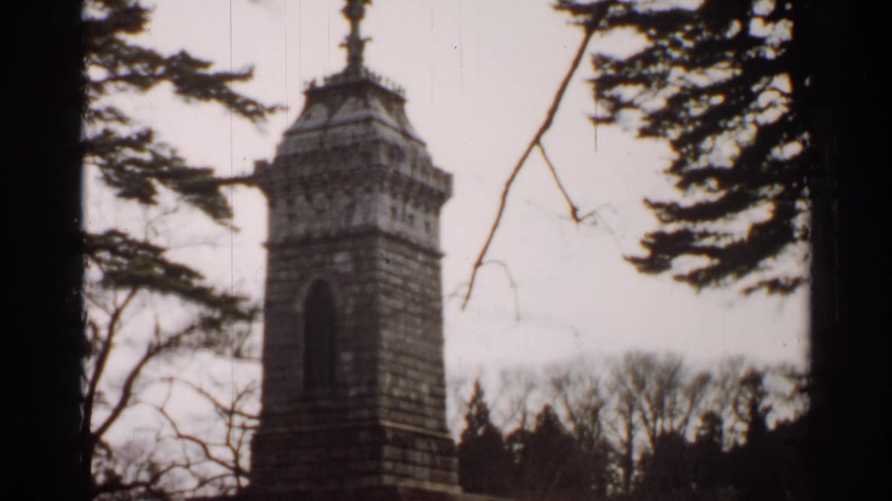 1952 Japan 8mm frame with a stone tower monument and perched bird form, seen between dark trunks and winter branches.