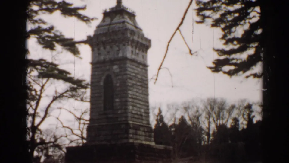 1952 Japan 8mm frame showing the stone monument closer in view, with the bird sculpture partly obscured by branches.
