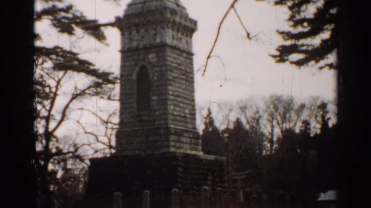1952 Japan 8mm frame showing the monument from a steady viewpoint, with branches crossing the sky and trees behind it.