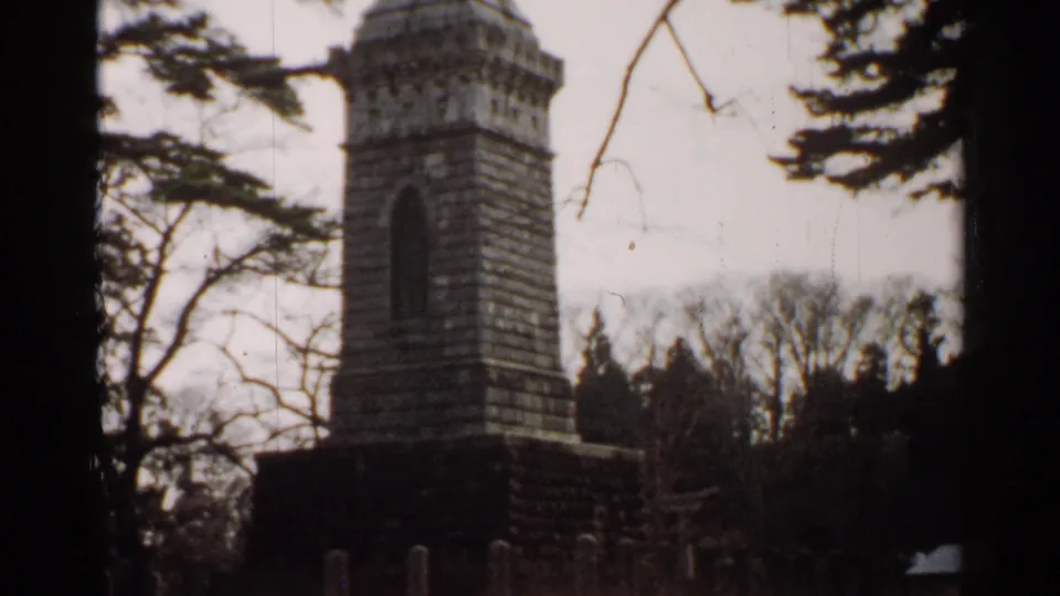 1952 Japan 8mm frame showing the monument from a steady viewpoint, with branches crossing the sky and trees behind it.