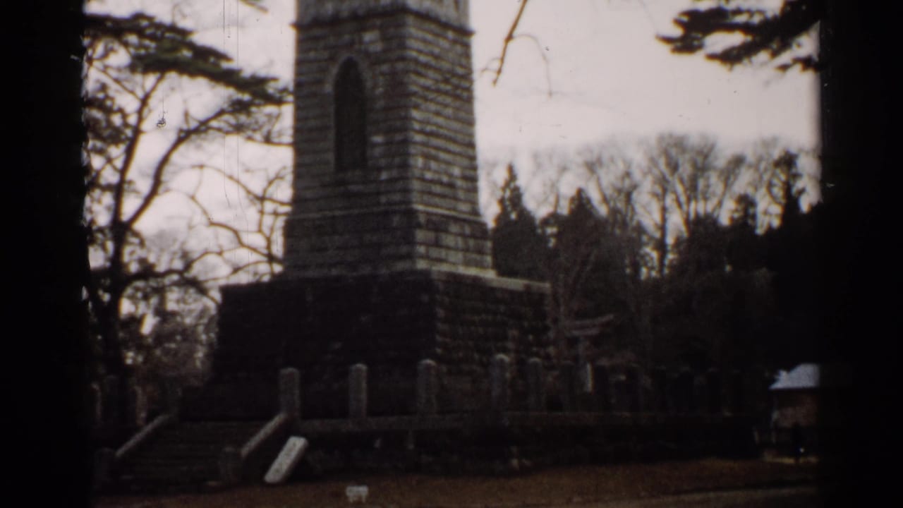 1952 Japan 8mm view of a stone monument enclosure with steps, upright markers, trees, and a small structure nearby.