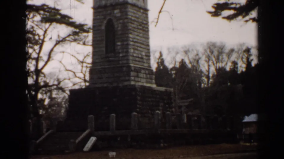 1952 Japan 8mm view of a stone monument enclosure with steps, upright markers, trees, and a small structure nearby.