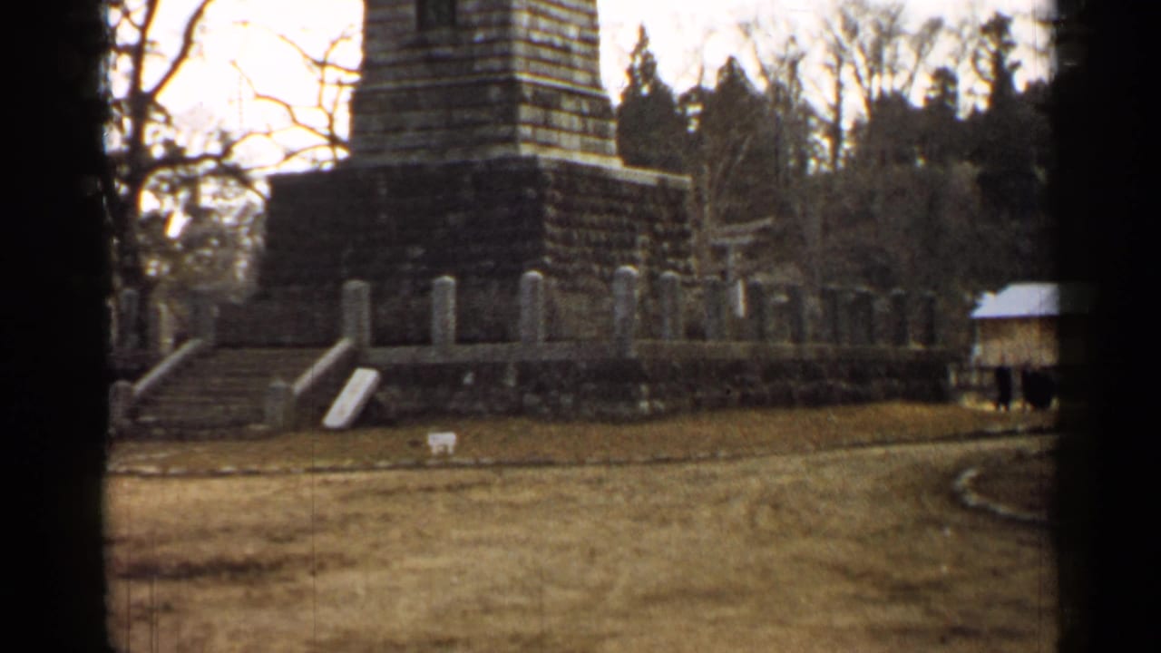 Stone monument and markers beside a paved path with a small dark figure in the distance.