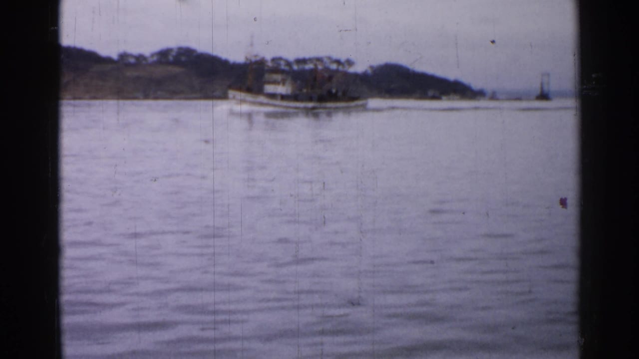 The tugboat continues along calm water past a low shoreline, with soft focus and visible 8mm film wear.