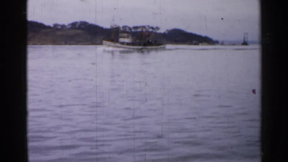 The tugboat continues along calm water past a low shoreline, with soft focus and visible 8mm film wear.