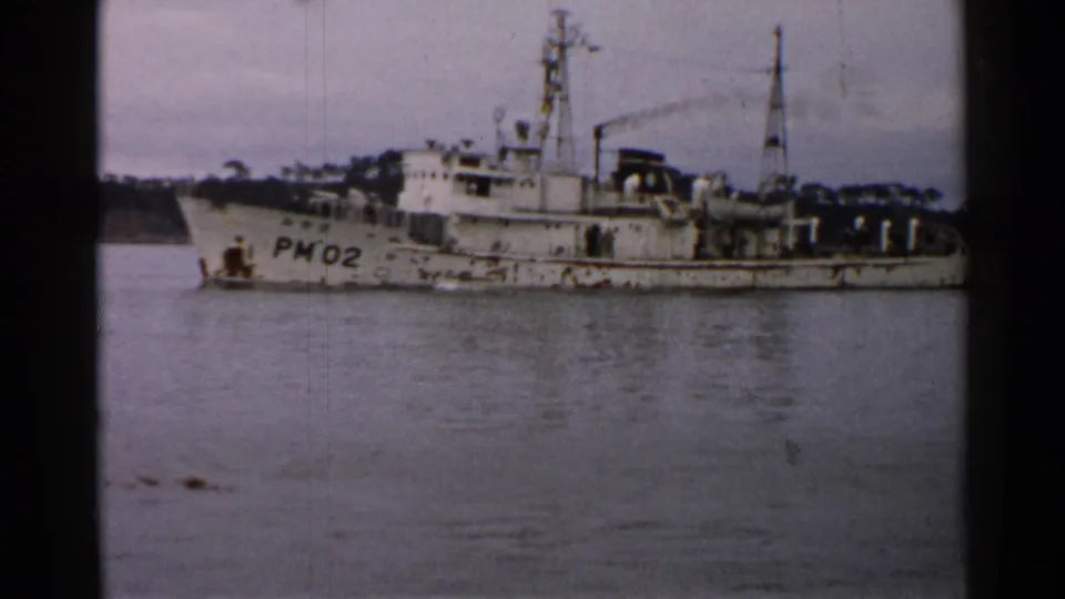 1952 Japan 8mm frame showing a weathered white naval vessel marked PM02 at anchor under an overcast sky.