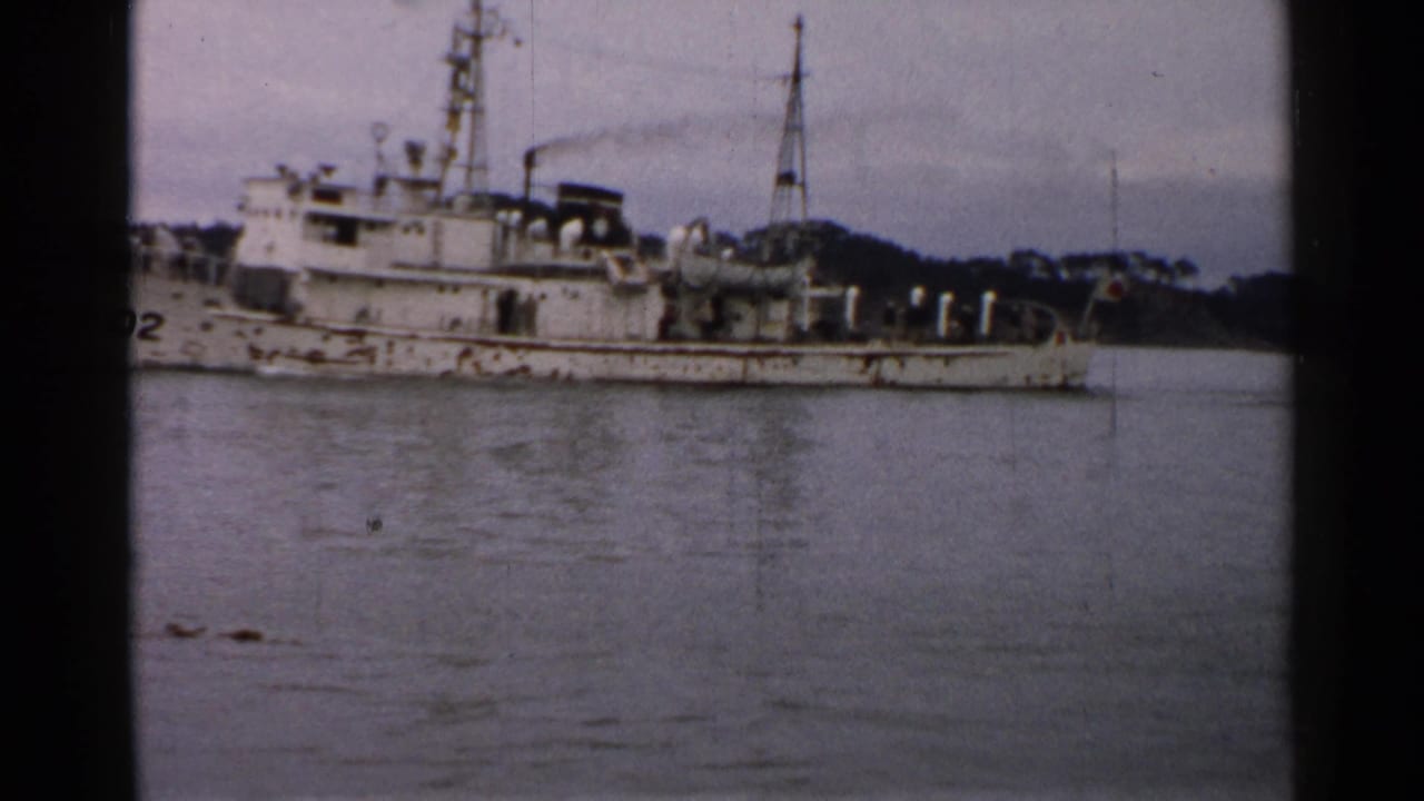 1952 Japan home-movie frame with the PM02 vessel partly cropped, showing deck fittings, mast, stern area, and still water.