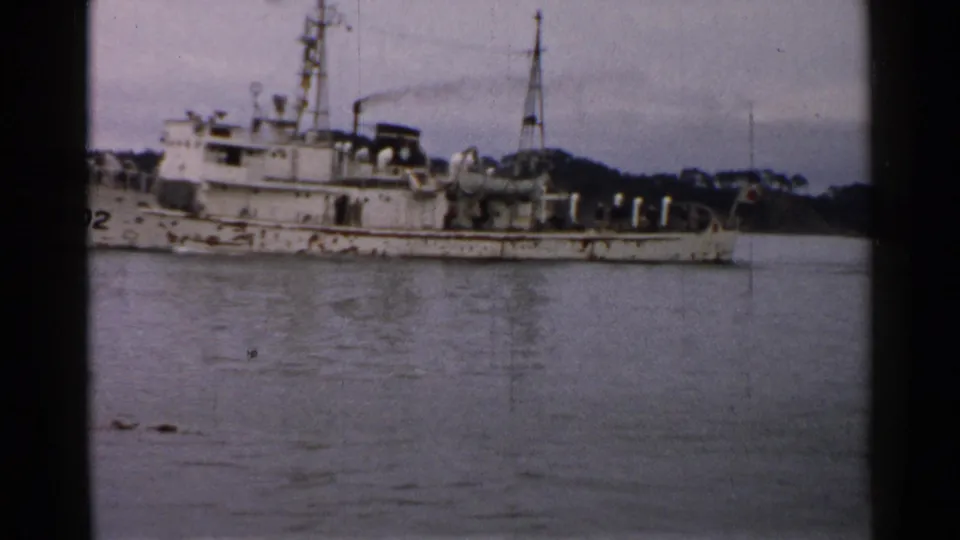 1952 Japan home-movie frame with the PM02 vessel partly cropped, showing deck fittings, mast, stern area, and still water.