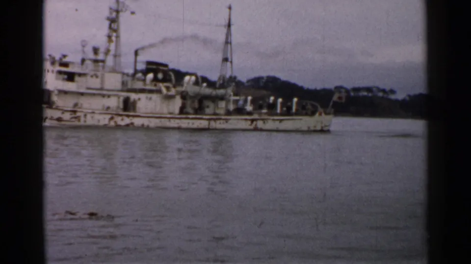 Final 1952 Japan frame showing the weathered PM02 vessel partly cropped, with rigging, deck equipment, calm water, and wooded shore.