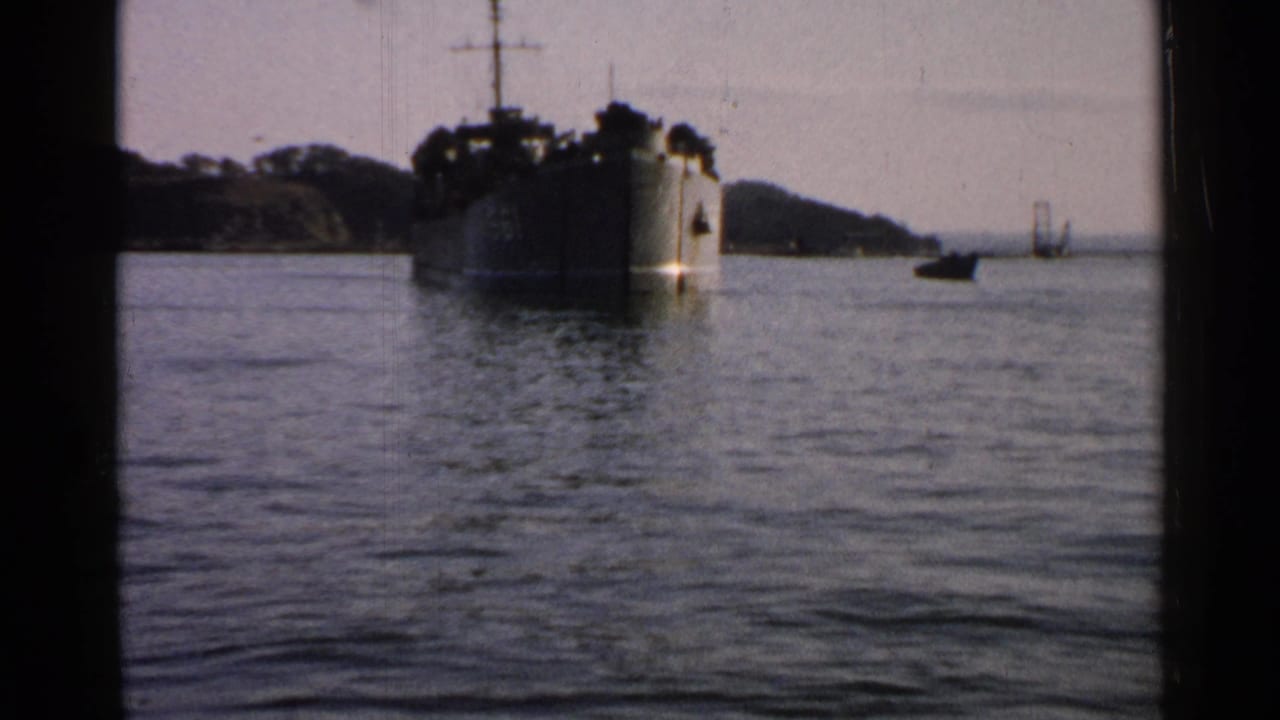 1952 Japan 8mm still of a large vessel near a wooded shoreline, filmed from across calm water with muted color.