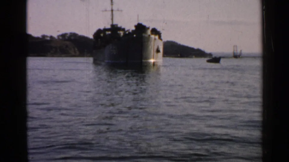 1952 Japan 8mm still of a large vessel near a wooded shoreline, filmed from across calm water with muted color.