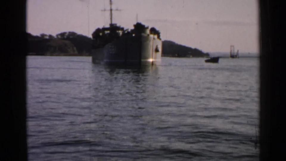 1952 Japan frame showing the large ship on harbor water with a small boat and distant bridge-like structure to the right.