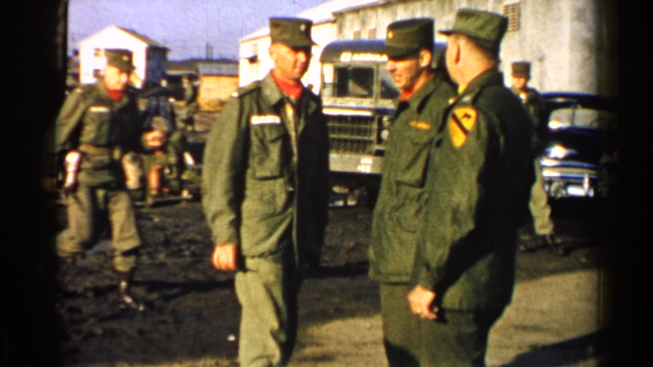 U.S. Army personnel at a Japan military base in 1952, framed with a truck, car, low buildings, and muddy ground.