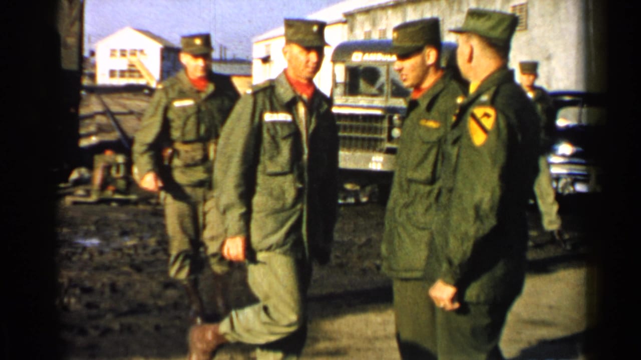 U.S. Army soldiers in 1952 Japan appear in olive uniforms near trucks and low buildings in a muddy compound.