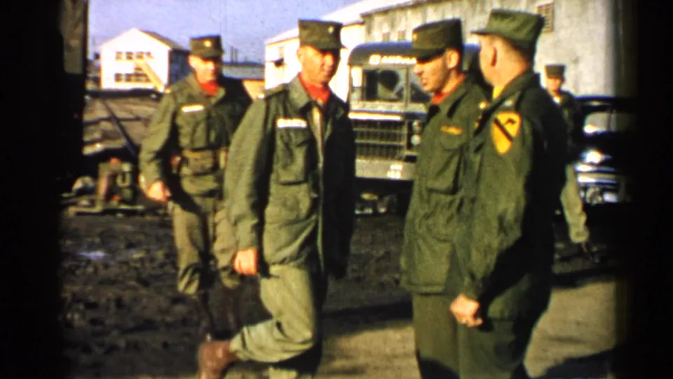 U.S. Army soldiers in 1952 Japan appear in olive uniforms near trucks and low buildings in a muddy compound.