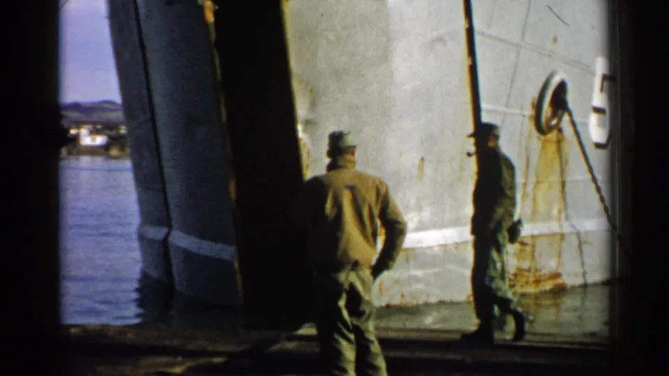 Two soldiers appear beside a large ship hull near water, extending the Japan 1952 Army footage into a dockside setting.