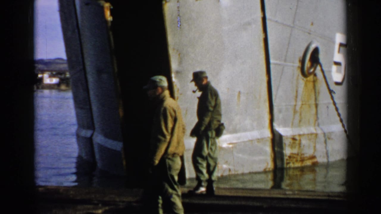 Two uniformed men appear near a weathered white hull in Japan 1952 footage, with one partly in shadow and water behind them.