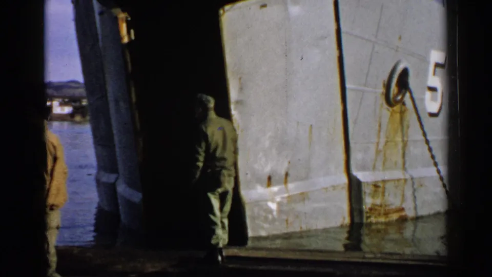 A uniformed man moves into a dark deck area beside a white vessel hull with the number 5 visible in 1952 Japan footage.