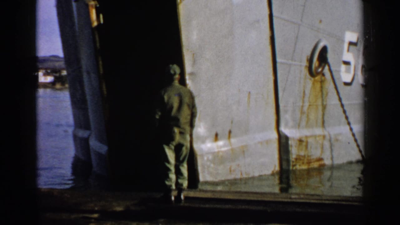Uniformed man walks toward an open gray ship ramp beside water.