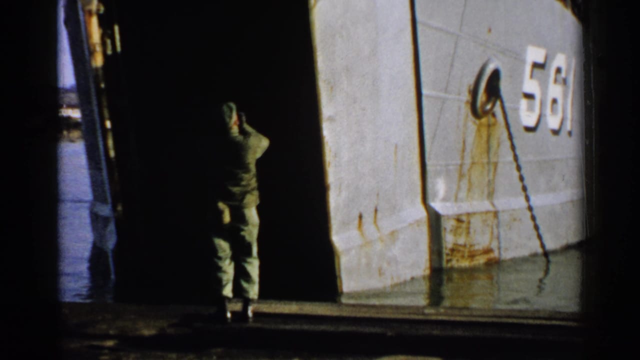 Uniformed man stands at the ramp opening beside the weathered hull marked 561.