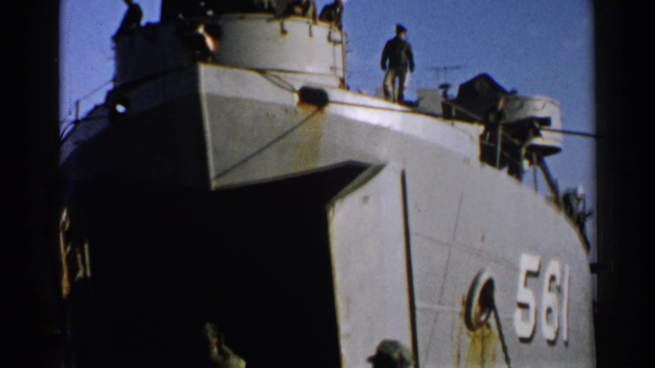 Numbered vessel bow with men standing on the deck and superstructure under a blue sky.
