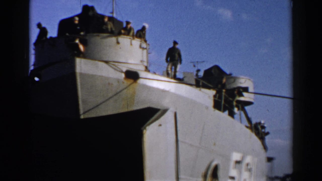 Archival 8mm frame from Japan showing men standing on a military-looking vessel with the number 561 on the hull.