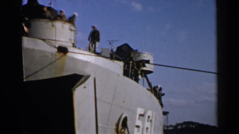 1952 Japan 8mm frame showing a numbered vessel with uniformed men on deck and distant land low in the background.