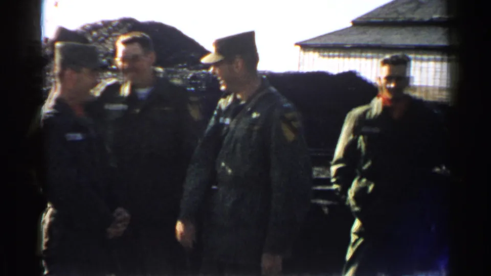 1952 Japan 8mm frame of uniformed men standing and smiling near a coal pile, rail yard tracks, and a small building.