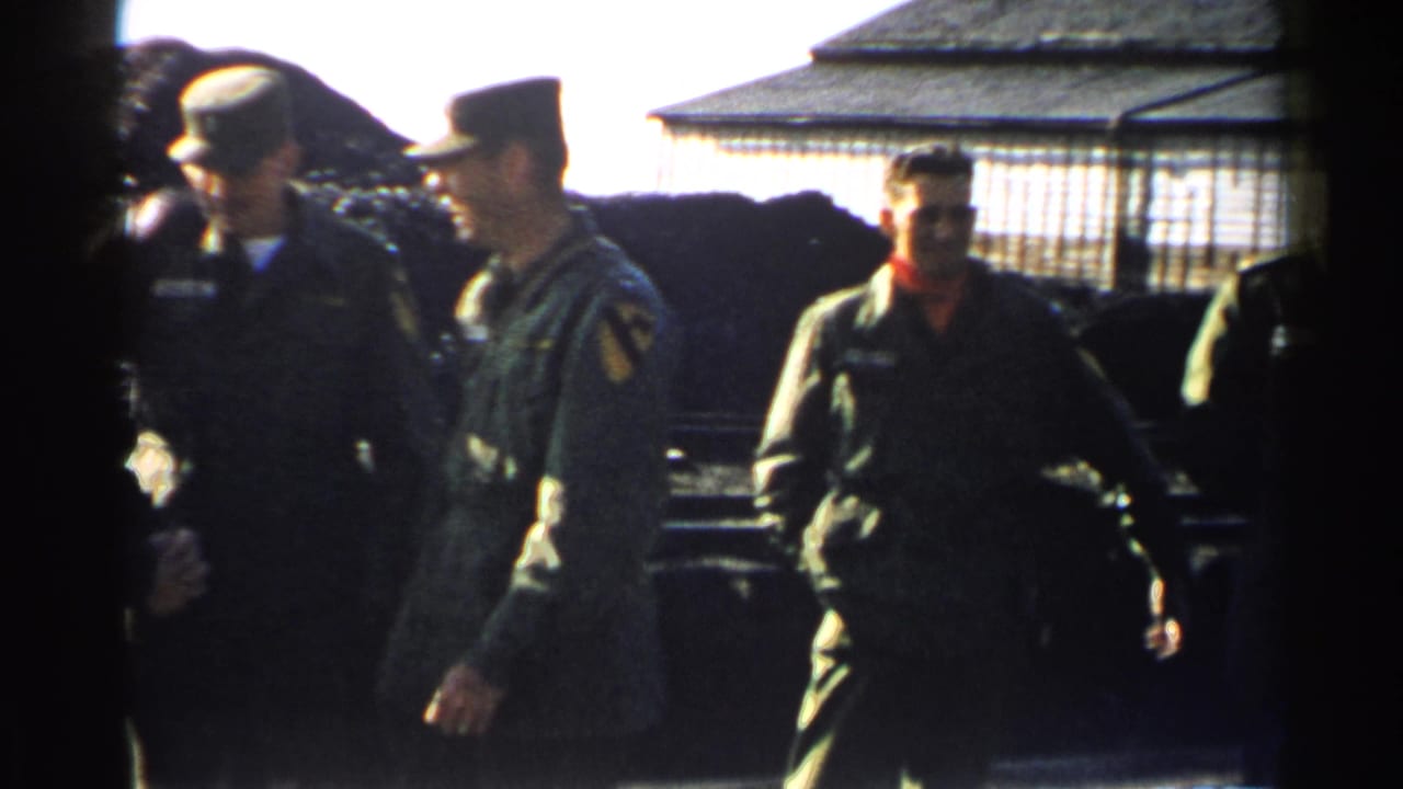 Several uniformed men stand and walk near a wire-fenced enclosure.