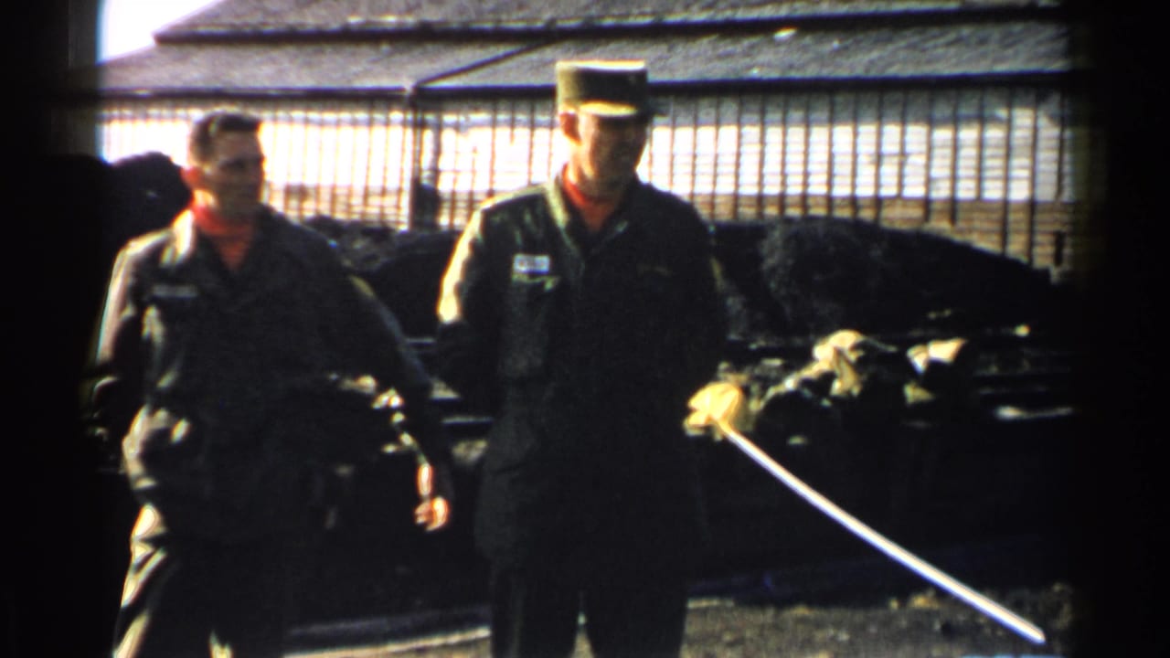 In Japan 1952 home-movie footage, two uniformed men stand near a fenced area with a low building behind them.