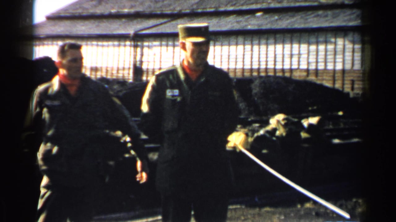 Two uniformed men stand in the same outdoor Japan 1952 setting, partially shadowed beside a fence and building.