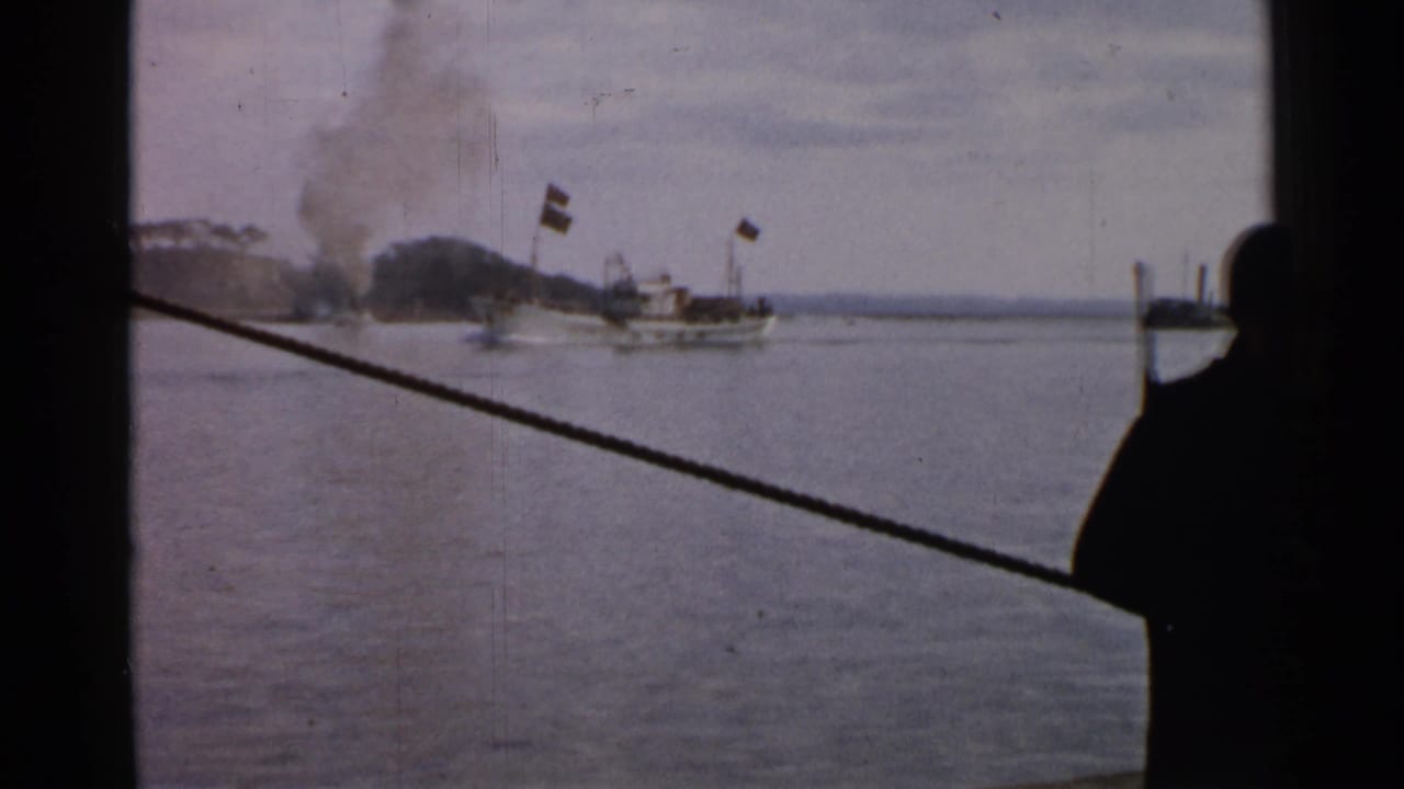 1952 Japan 8mm frame showing a smoking ship at sea, distant shoreline, mast flags, and a diagonal rope from the filming vessel.