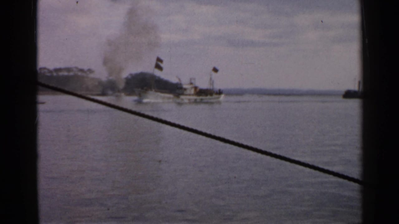 1952 Japan 8mm frame with a smoking vessel on calm water and a silhouetted passenger or crew member in the foreground.
