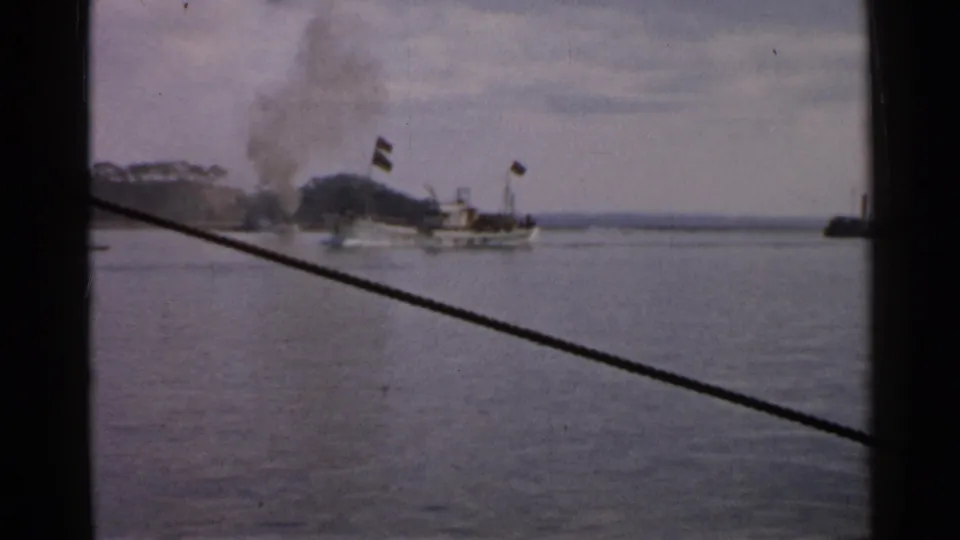 1952 Japan 8mm frame with a smoking vessel on calm water and a silhouetted passenger or crew member in the foreground.