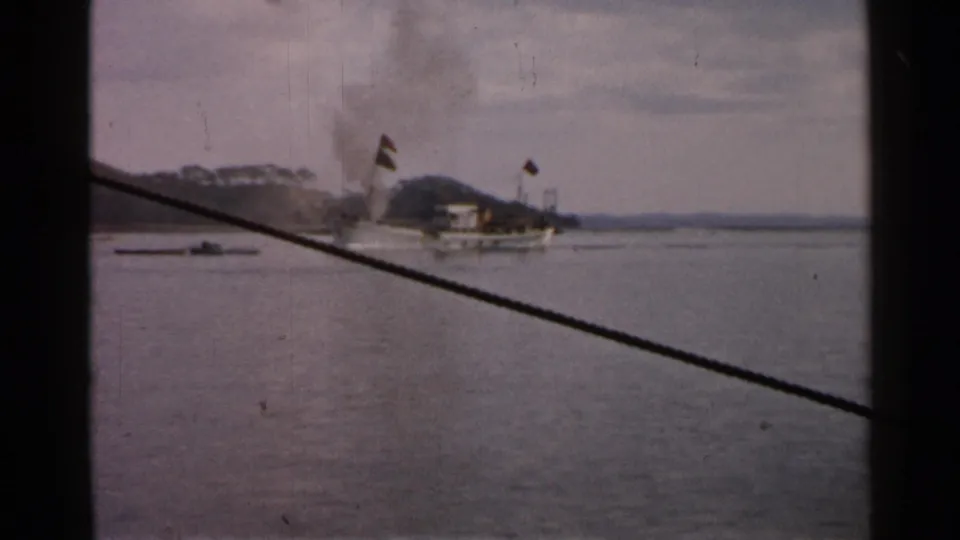 1952 Japan 8mm frame of a smoking ship passing on calm water, partly framed by rope and dark edges from the filming position.