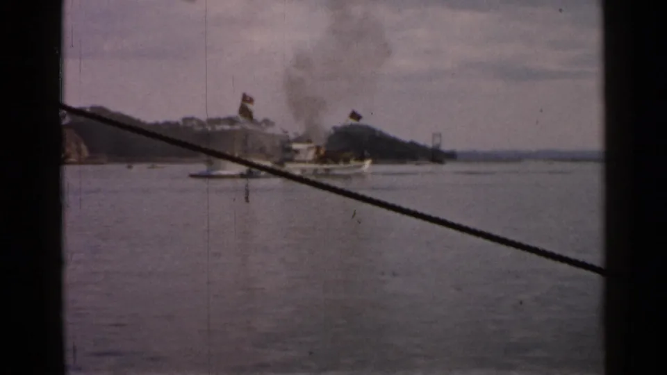 In this 1952 Japan home-movie frame, the small cargo vessel is nearer the shoreline with a plume of dark smoke rising above it.